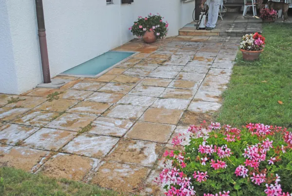 Dallage de pierre posé devant une maison, massifs de fleurs autour