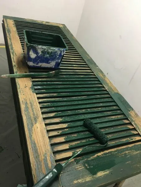 Persienne sur l’établi : à gauche le bois mis à nu, à droite la nouvelle couche verte